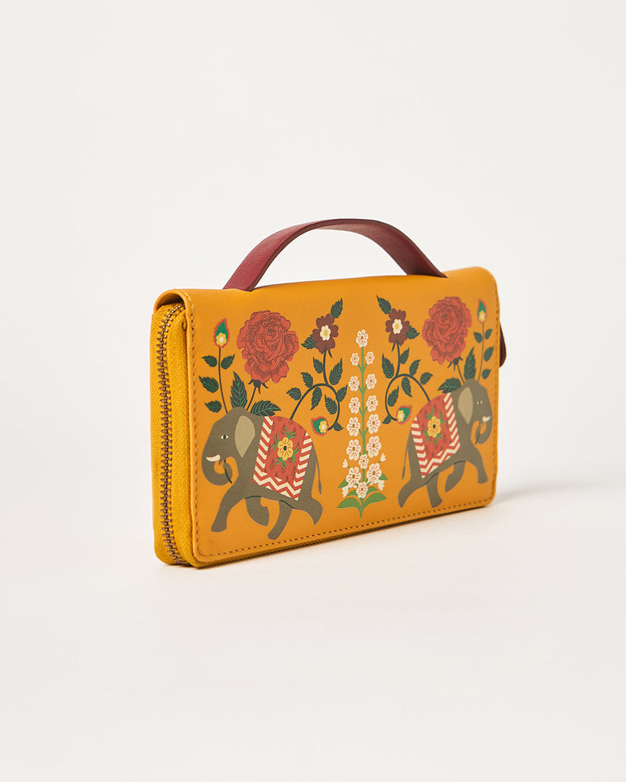 Mustard yellow wallet standing upright displaying elephant motifs and floral pattern with maroon top handle