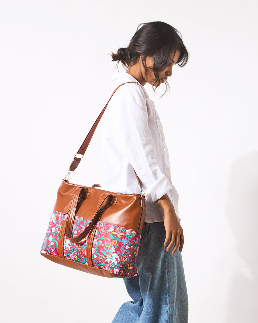 Woman carrying brown faux leather tote bag with colorful paisley and elephant print over her shoulder wearing white shirt and blue jeans