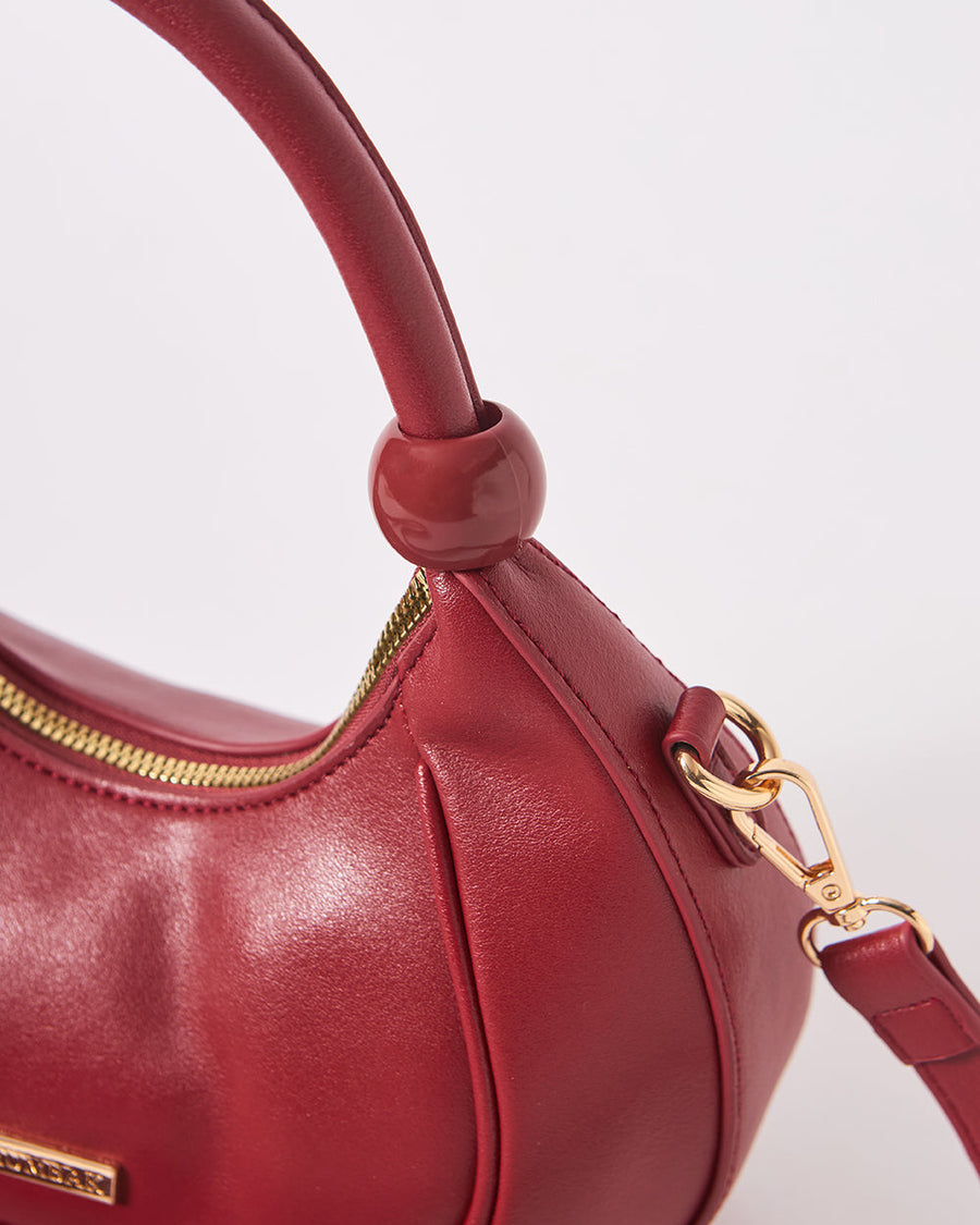 Close-up of the curved top handle with signature round bead detail on the maroon vegan leather crescent handbag.