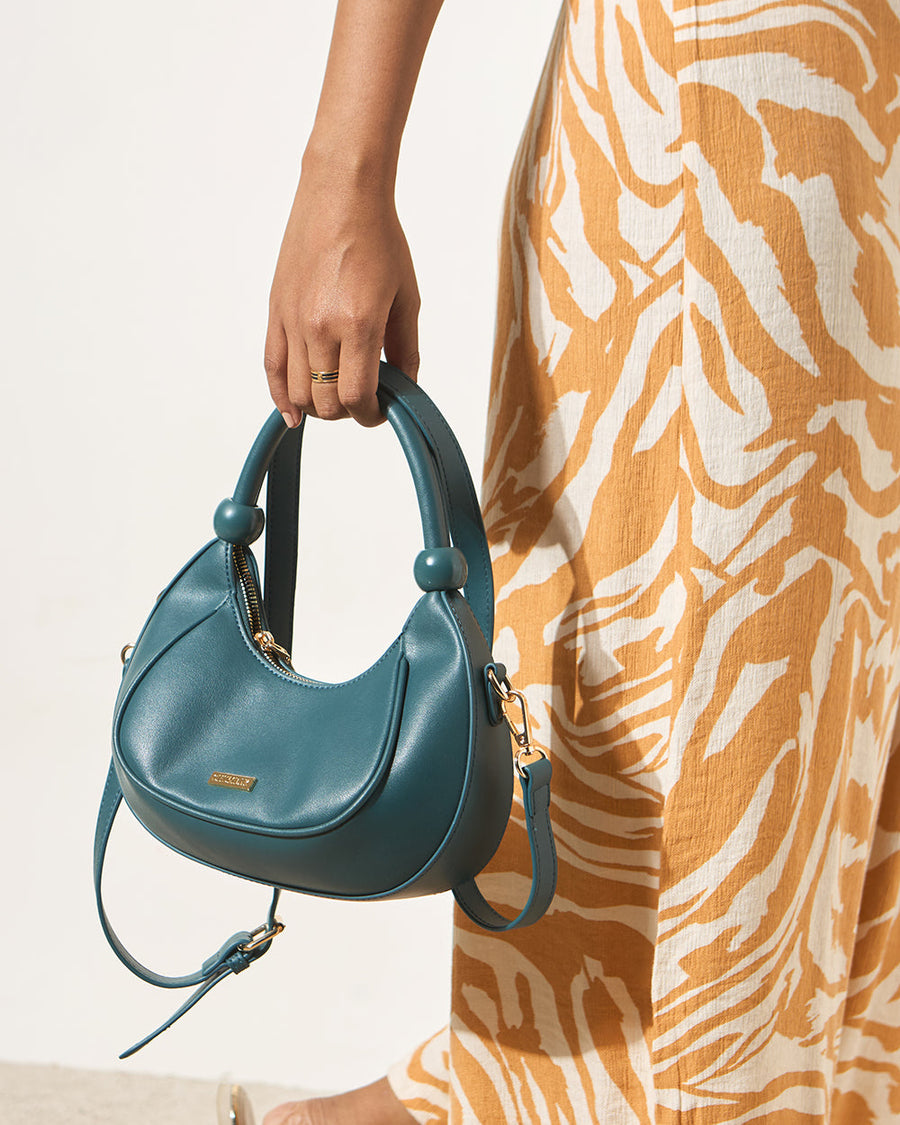 Close-up of woman holding the deep teal crescent handbag by its top handle