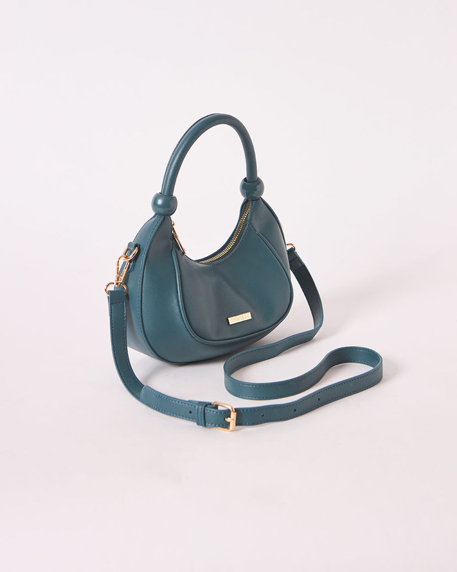 Side angle of deep teal handbag with adjustable crossbody strap on white background