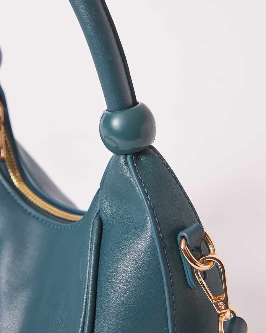 Close-up of top handle detail and gold hardware attachment on vegan leather teal handbag
