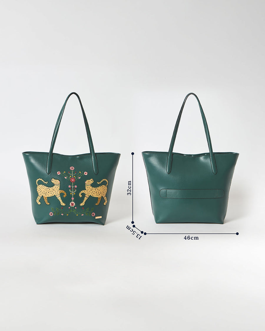 Back of deep green tote bag with strap fitted around suitcase handle, demonstrating travel convenience