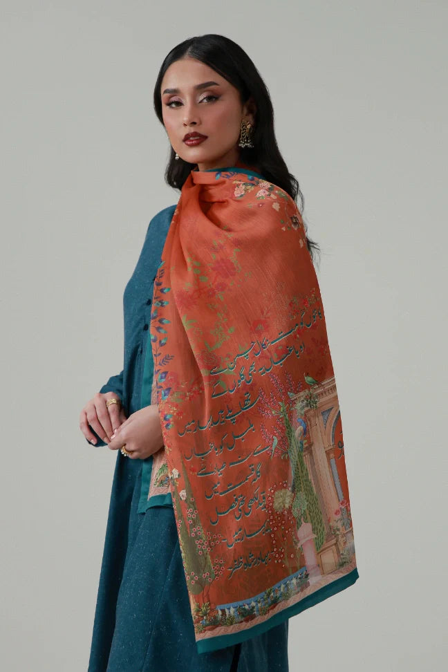 Woman wearing vibrant orange Baghban crinkle silk scarf with floral and calligraphy design over a blue outfit