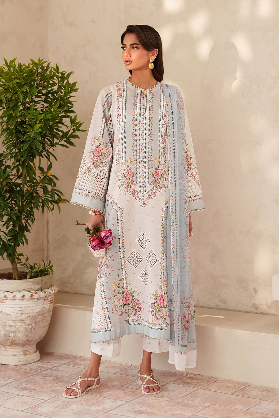 Front view of a woman wearing embroidered floral lawn suit in soft pastel colors, holding pink roses