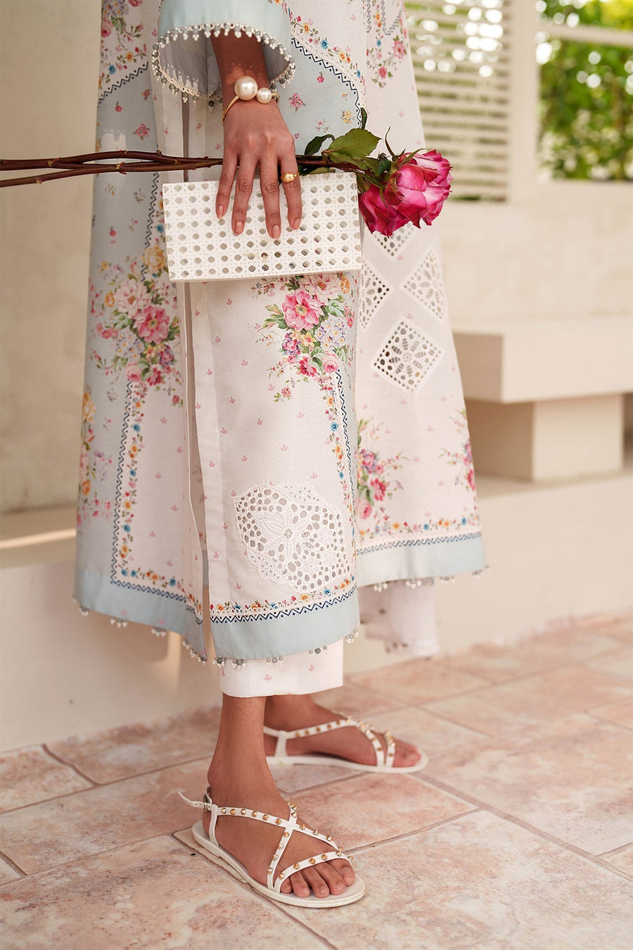 Close-up of embroidered sleeve and trouser hem with pearl bead trim, woman holding white clutch and pink roses