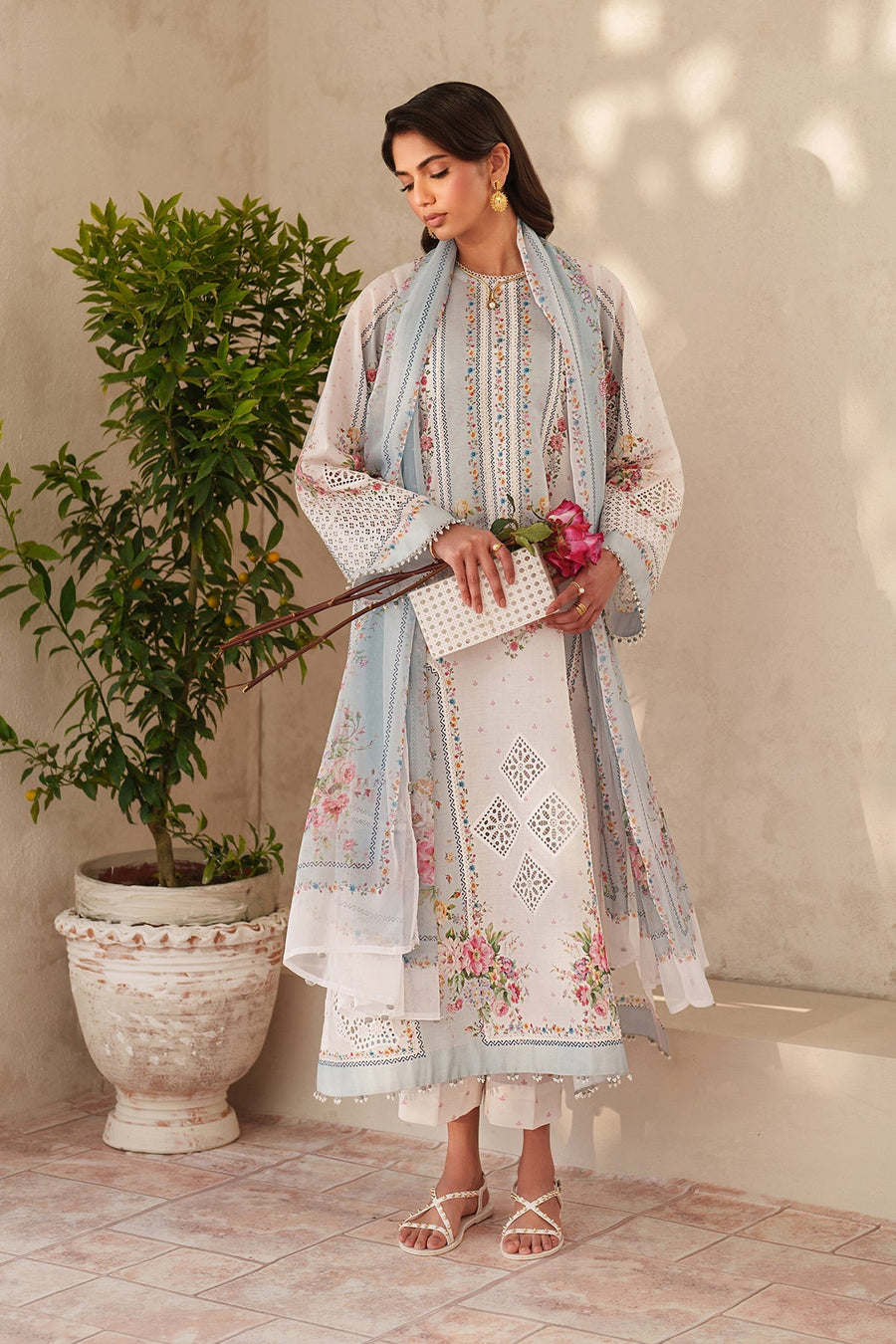 Full length front view of embroidered lawn suit with floral and cutwork details and printed dupatta, model holding pink roses