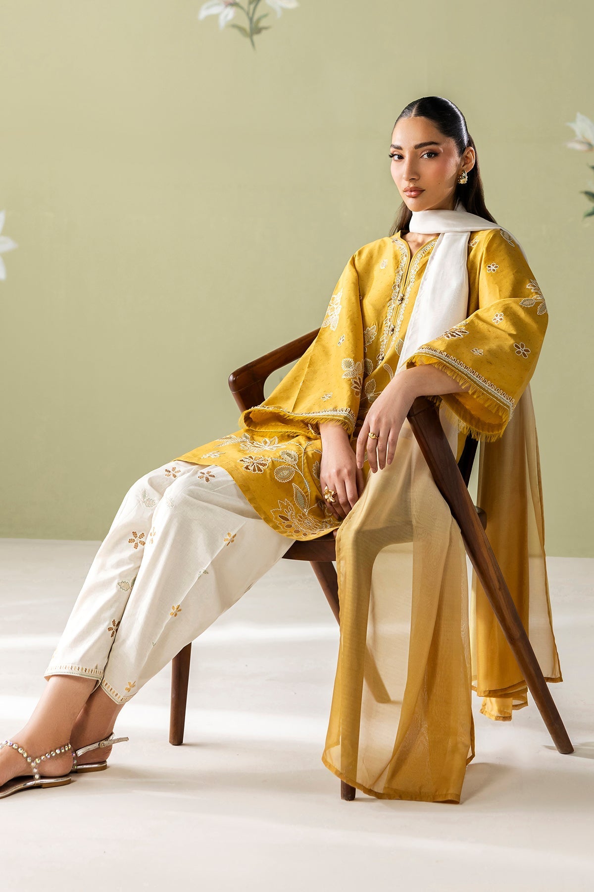 Model sitting on wooden chair showing full embroidered shirt, pants, and flowing ombré dupatta with styled sandals