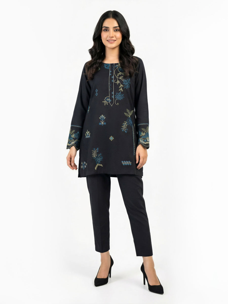 Front view of woman wearing embroidered black kurti with blue and green floral motifs paired with black trousers and black heels