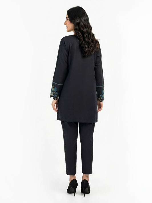 Back view of woman modeling plain black kurti and tapered trousers with scalloped embroidered sleeve cuffs