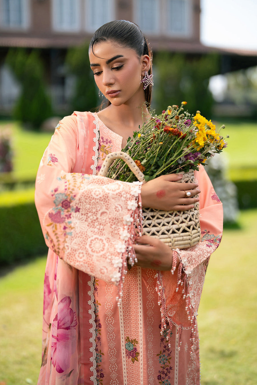 Close-up of woman holding floral basket wearing embroidered peach lawn suit with bead details