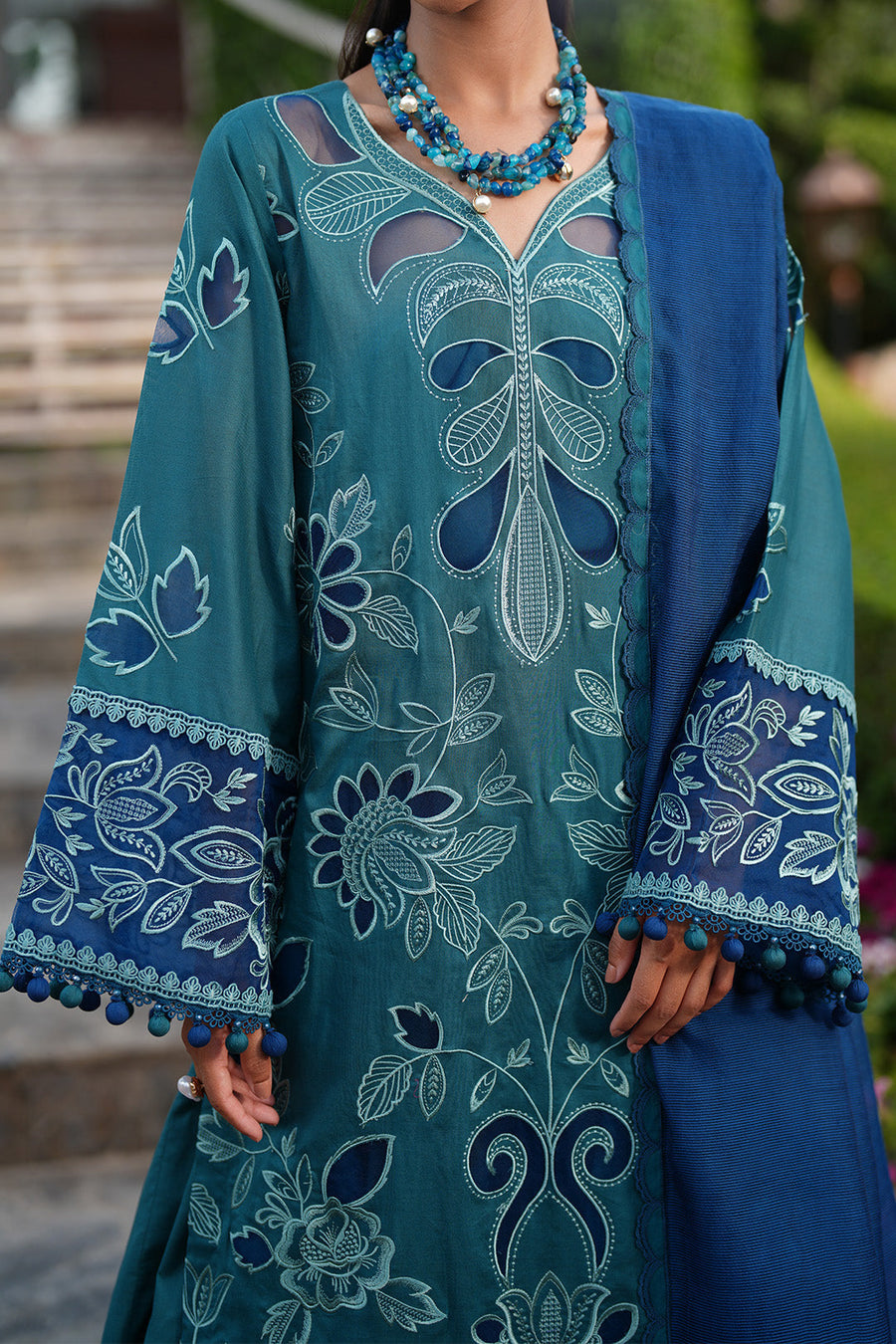 Detail view of sleeve embroidery and blue pompom trim on high-quality lawn fabric