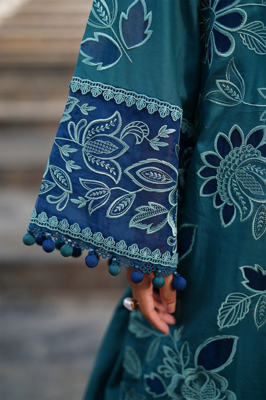 Close frontal view displaying rich embroidery pattern with blue and white thread on teal-green fabric