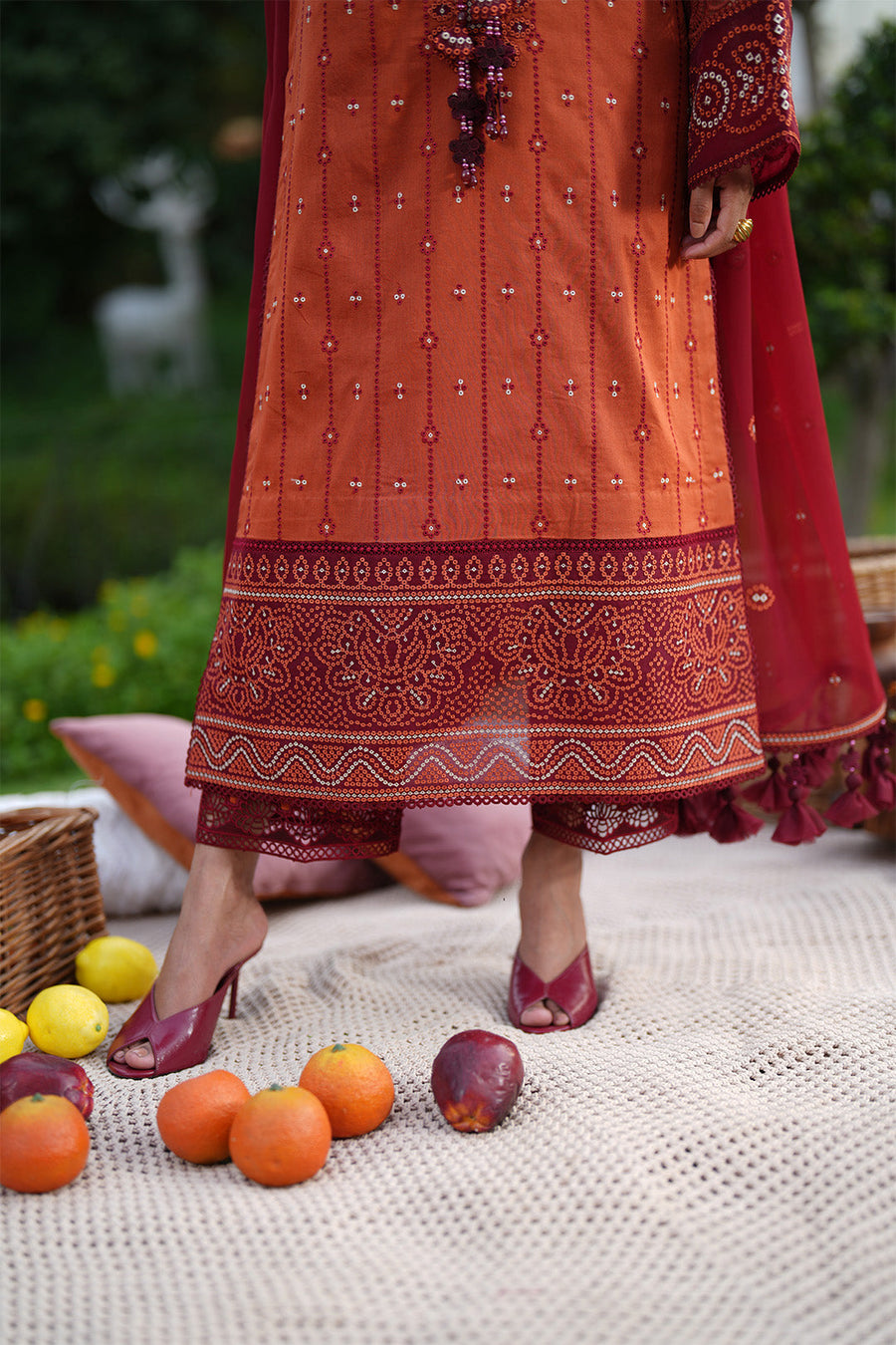 Woman wearing rust and maroon embroidered suit in garden setting with fruits around