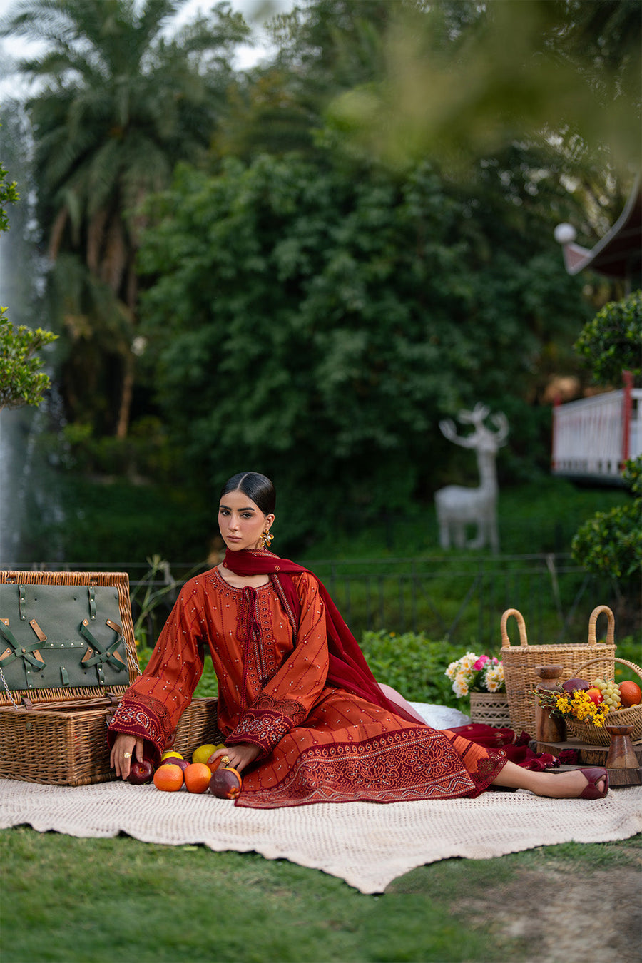 Woman seated outdoors wearing rust orange embroidered lawn with maroon dupatta and trousers