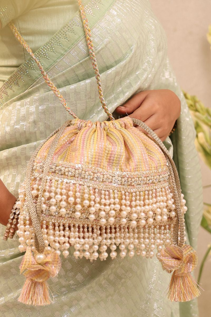 Amari Pearl Embellished Potli Bag in multicolor organza with pearl fringe and braided drawstring held by a woman wearing a shimmering light green traditional outfit.