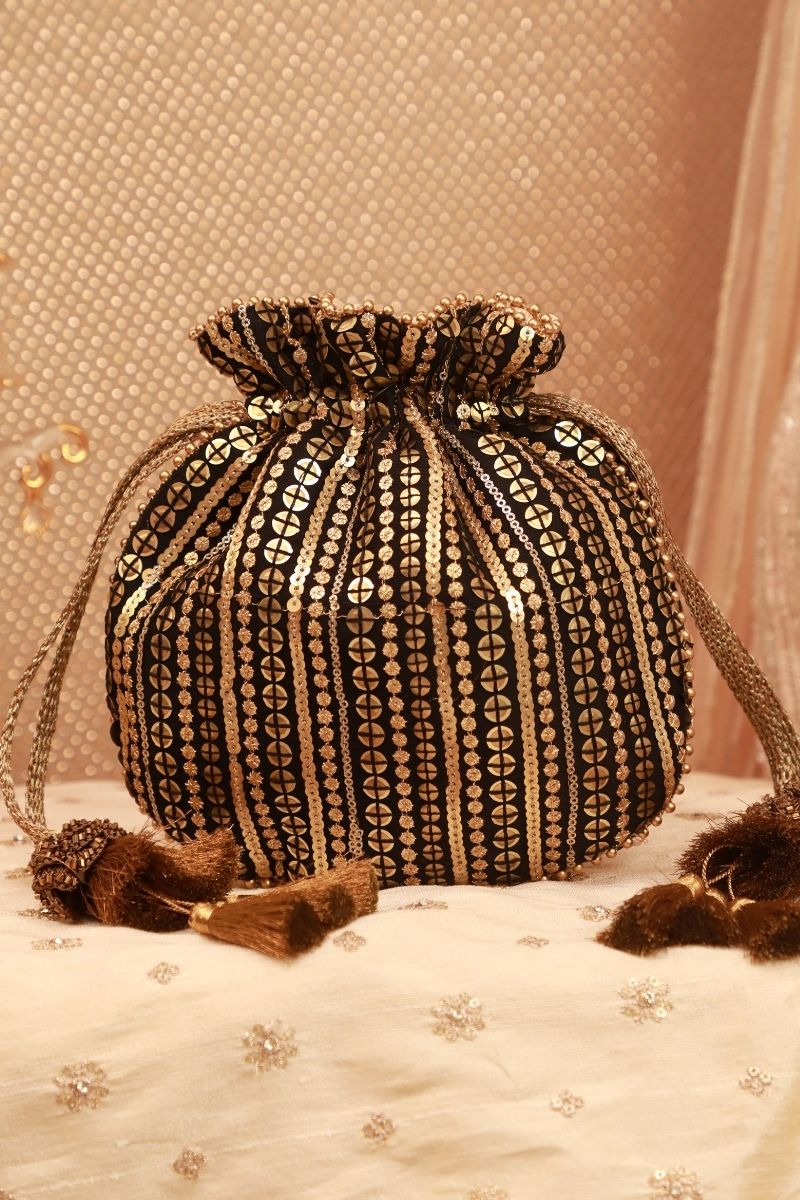 Black potli bag with vertical gold sequin embroidery and drawstring tassels against a beige fabric background