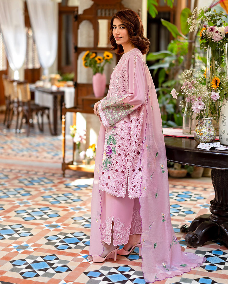 Side view of a woman in a pastel pink embroidered lawn outfit showing detailed embroidery and lacework on the sleeves and trousers, complemented by a floral embroidered dupatta.