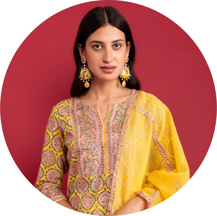Woman wearing a yellow and patterned outfit with earrings against a red background