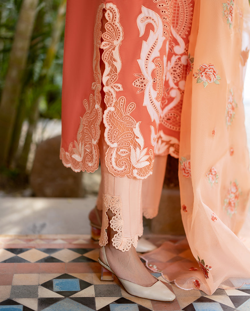 Close-up of the scalloped lace and cutwork detail on the hem of the peach trousers and embroidered lawn shirt.