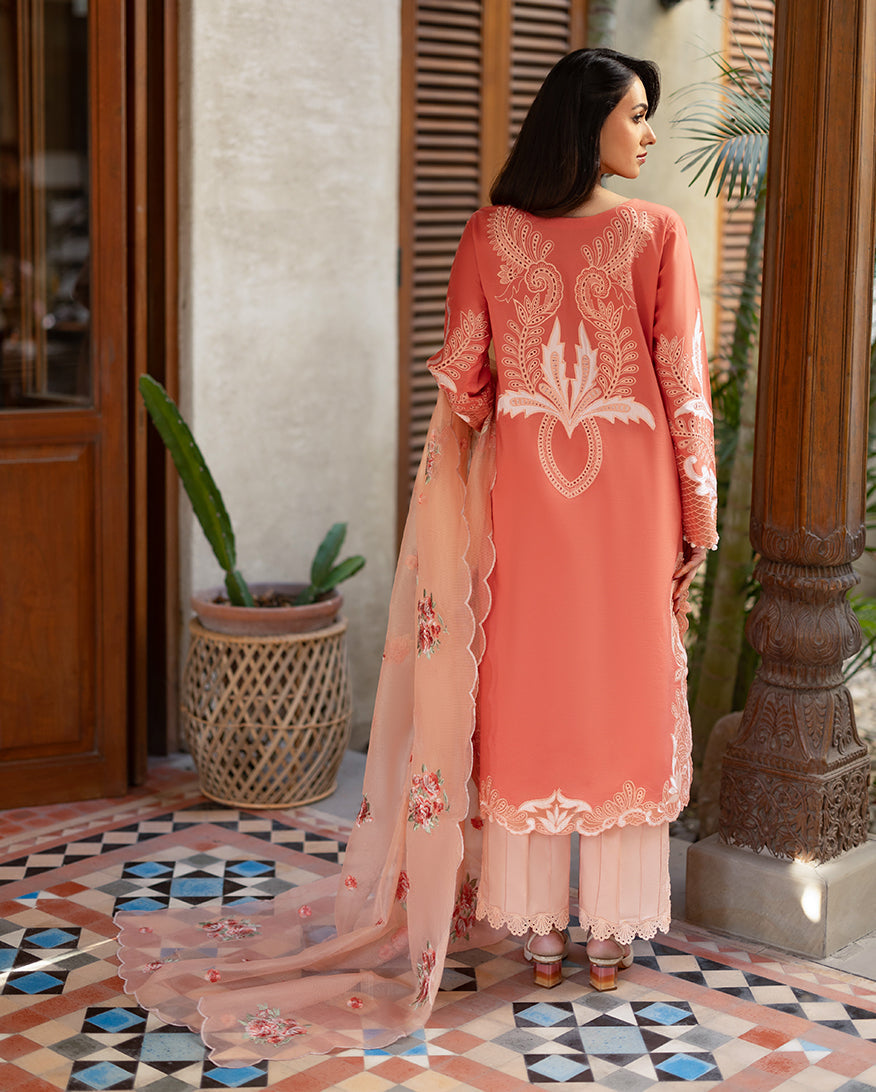 Rear view of the embroidered coral lawn shirt showing symmetrical white embroidery on the back, paired with peach trousers and an embroidered peach net dupatta.