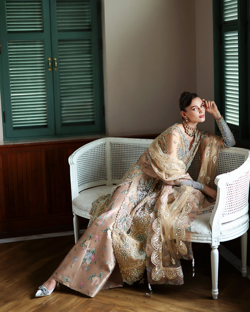 Model seated on white vintage sofa wearing full embellished formal dress with embroidered net dupatta draped elegantly