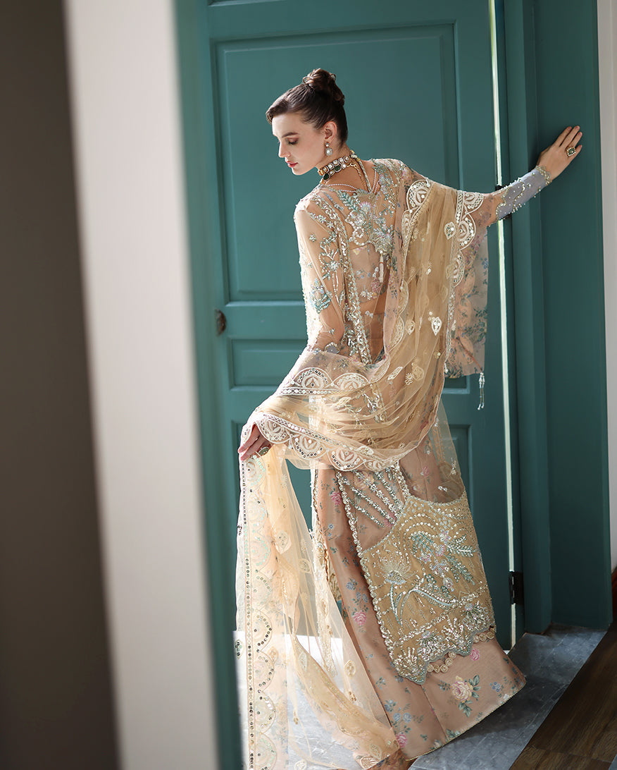 Back view of model holding sheer embroidered dupatta with scalloped edges, highlighting detailed hand embellishments on the net dress