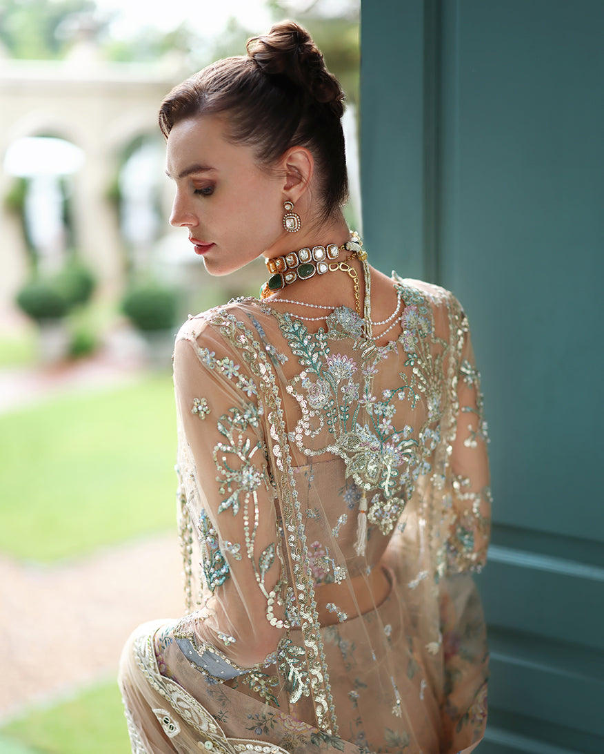 Side back view of model displaying elaborate floral embroidery and delicate beadwork on sheer net fabric in soft natural light