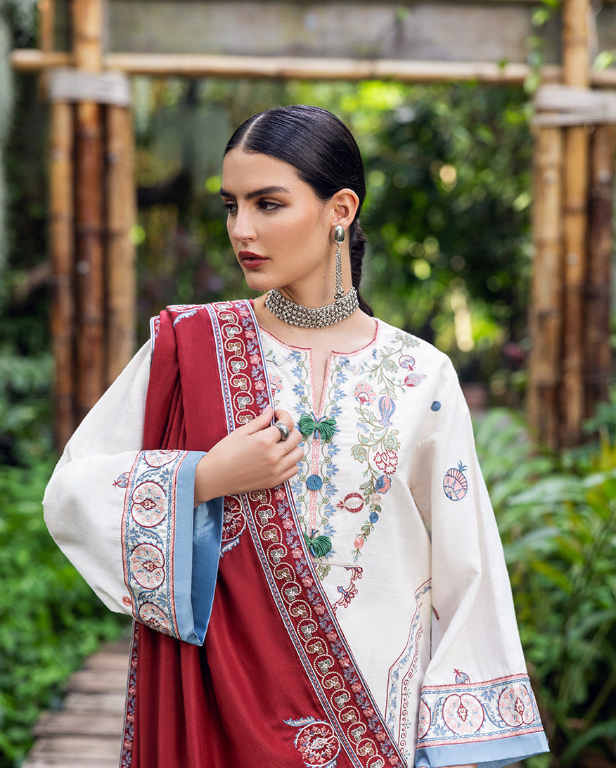 Close-up of woman wearing white embroidered Karandi kurta with detailed floral patterns and holding red embroidered shawl, adorned with silver jewelry