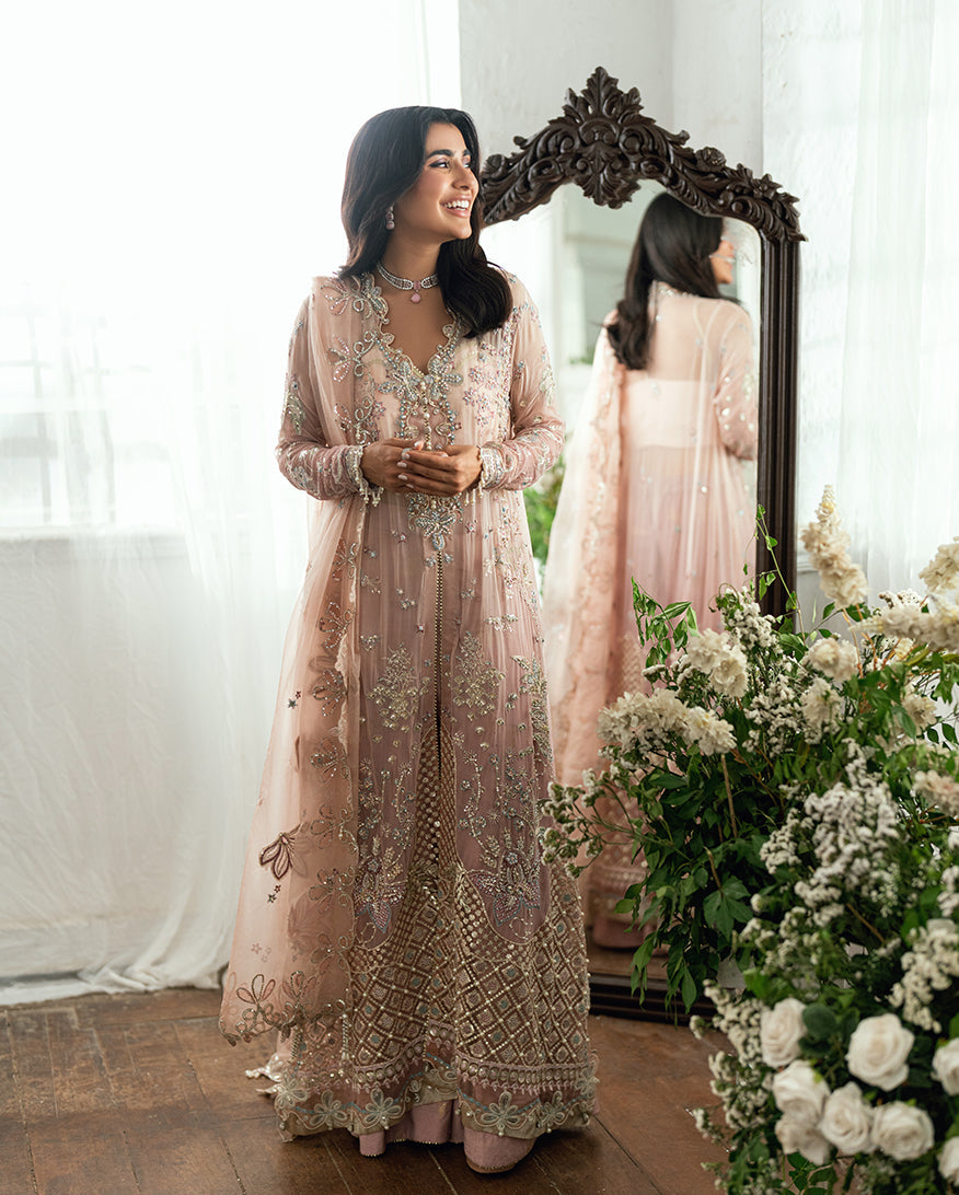 Woman smiling in the embroidered chiffon ensemble standing in front of a mirror with floral background