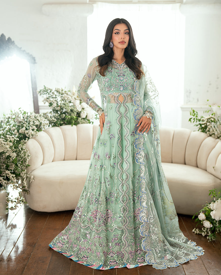 Woman wearing pastel mint green embellished chiffon dress standing beside cream sofa with floral décor