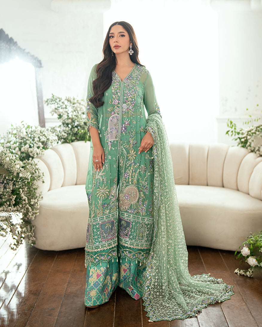 Full length view of woman dressed in embroidered green chiffon suit with wide printed trousers and embellished dupatta pooling on the floor