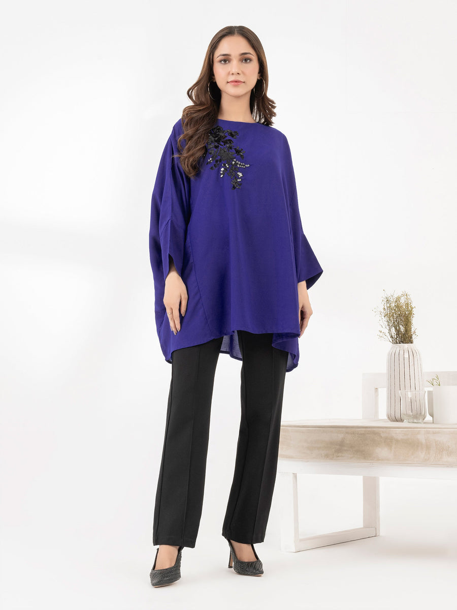 Front view of woman in royal blue embroidered loose fit top paired with black pants and high heels