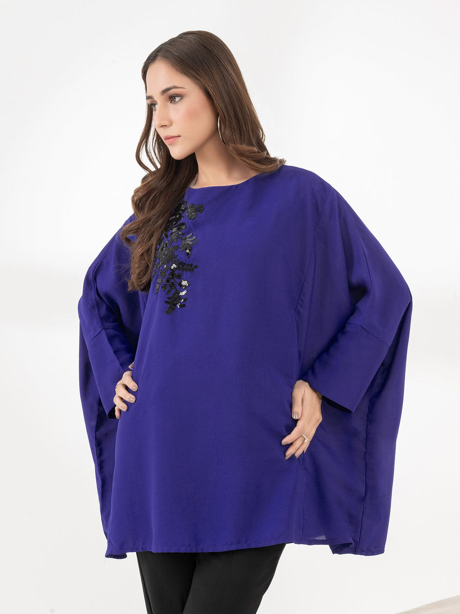 Woman wearing royal blue embroidered loose fit top with black floral sequin embroidery in a side pose