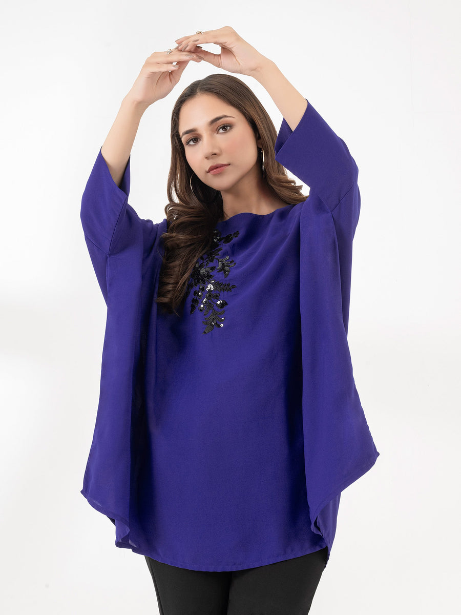 Woman with raised arms showcasing royal blue embroidered loose fit top with black floral sequin detail