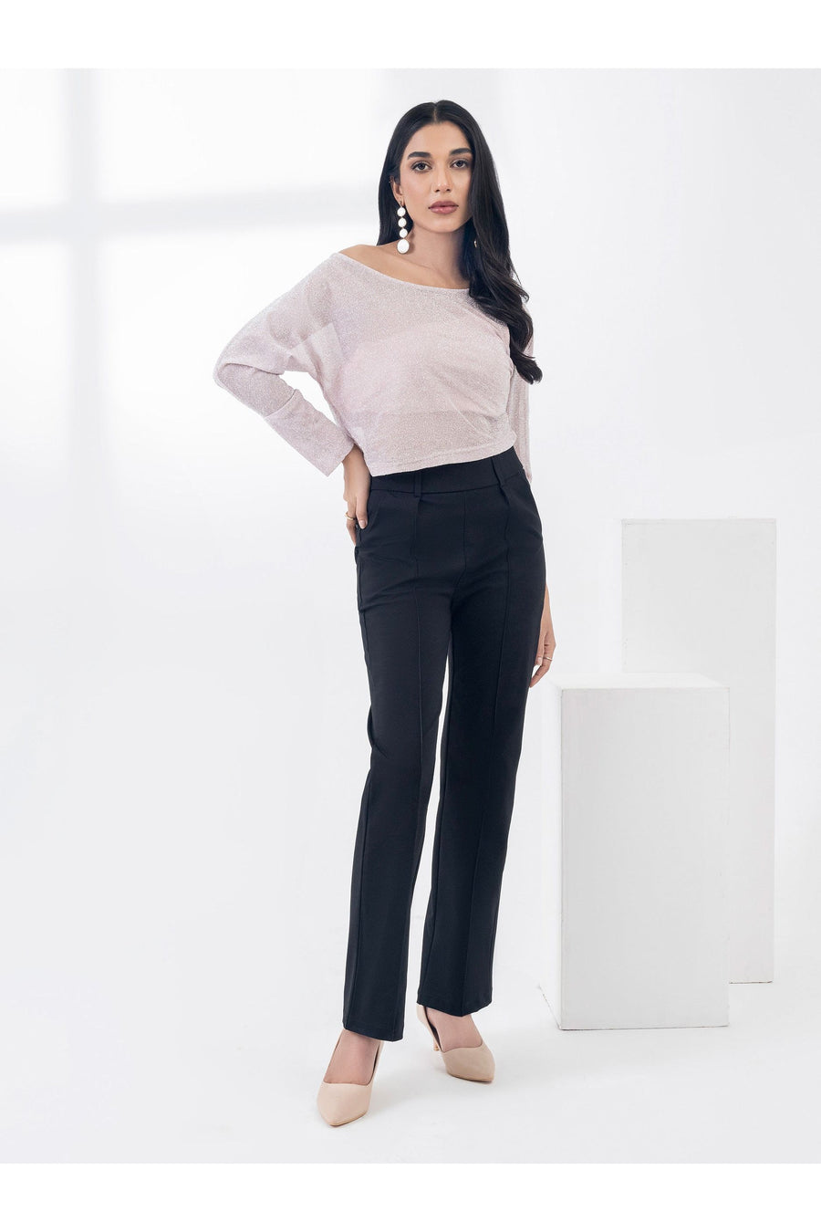 Model wearing a light pink off-shoulder dyed jersey top with black pants, standing in a bright room