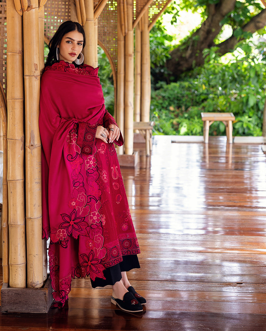 Posed side-angle view of woman enveloped in embroidered deep pink shawl showing floral scalloped edges and matching suit embroidery, standing in bamboo corridor