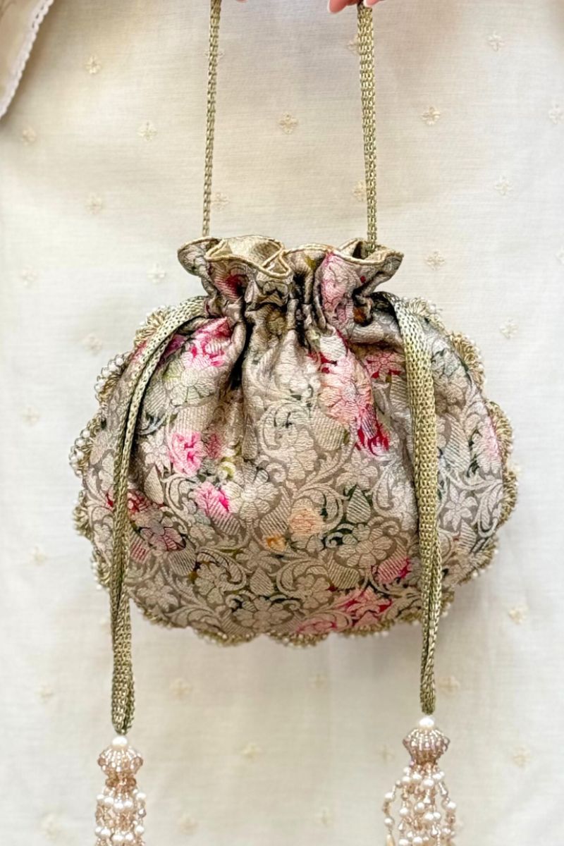 Close-up of a luxurious Banarasi silk potli bag in grey with embroidered floral patterns and pearl tassels.