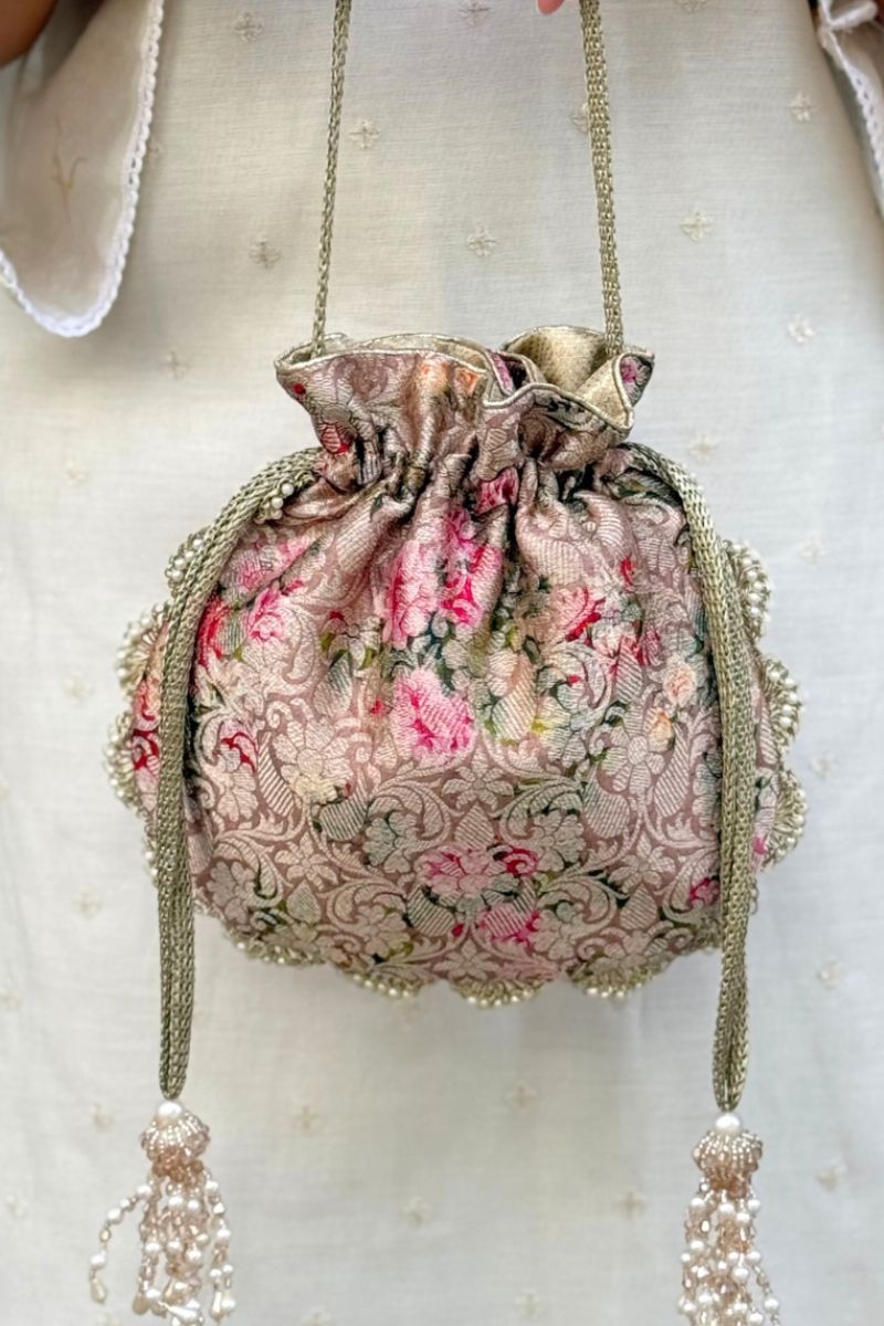 Close-up of a luxurious brocade potli bag with floral embroidery in pink and green, featuring pearl tassels on the drawstrings