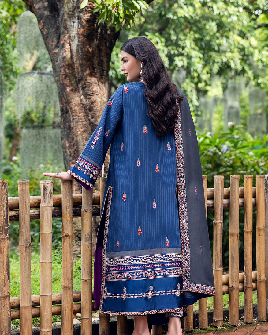 Back view of woman in blue striped karandi suit with small embroidered motifs and grey shawl draped over shoulder