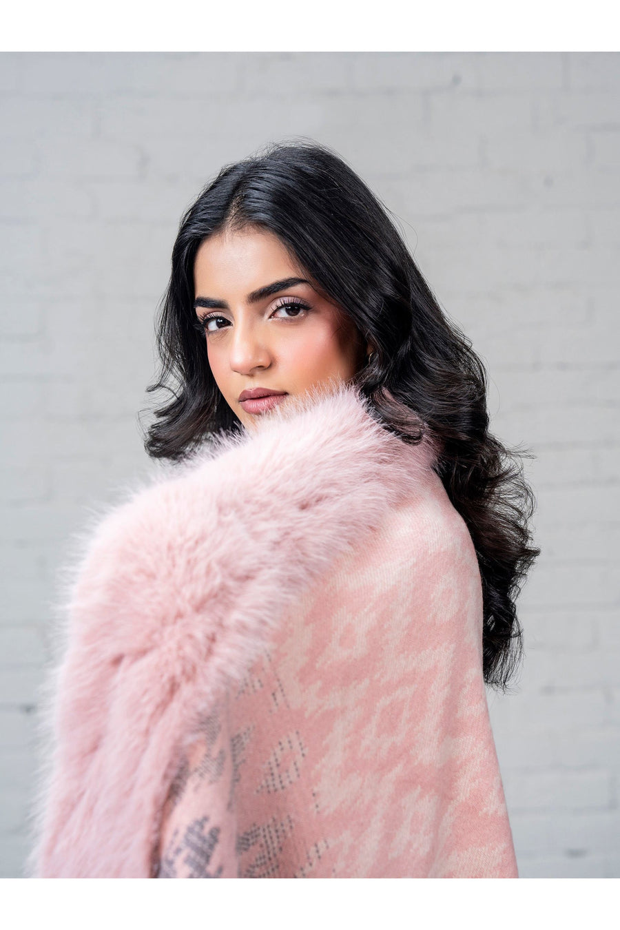 Detailed close-up of pink faux fur trim on wool cape with subtle pattern glimpsed, model looking over shoulder
