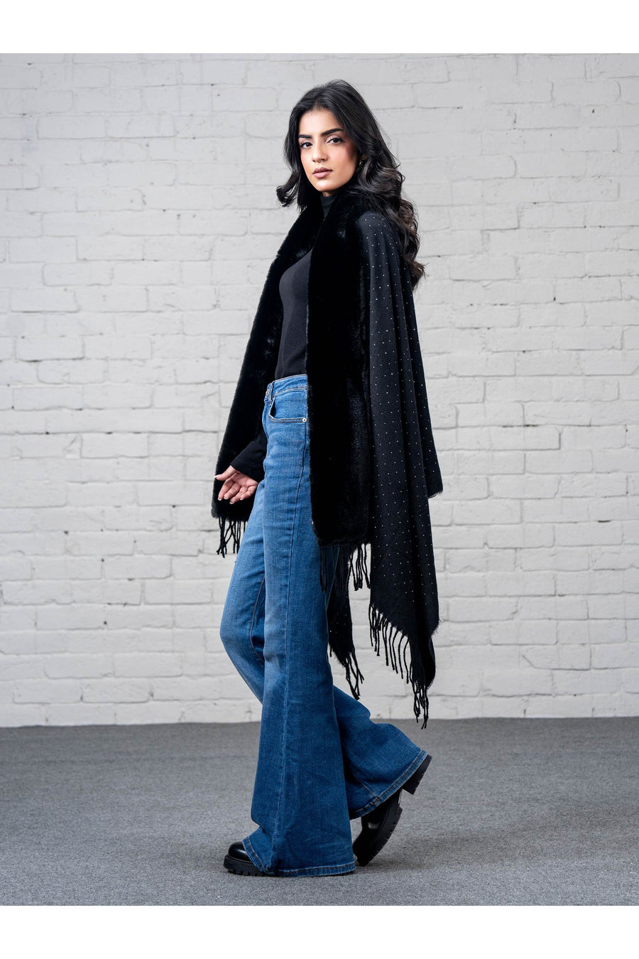 Side view of woman in black wool cape shawl with faux fur trim and fringed edges showcasing the elegant rhinestone pattern