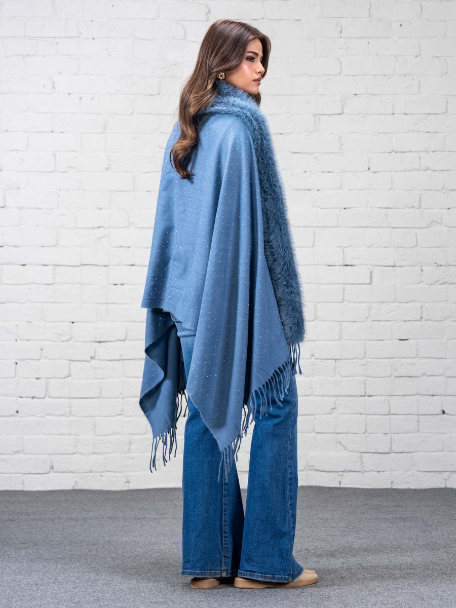 Back angle of the sky blue wool cape with faux fur trim and fringe, showcasing delicate rhinestone details, worn by woman in white turtleneck and blue jeans