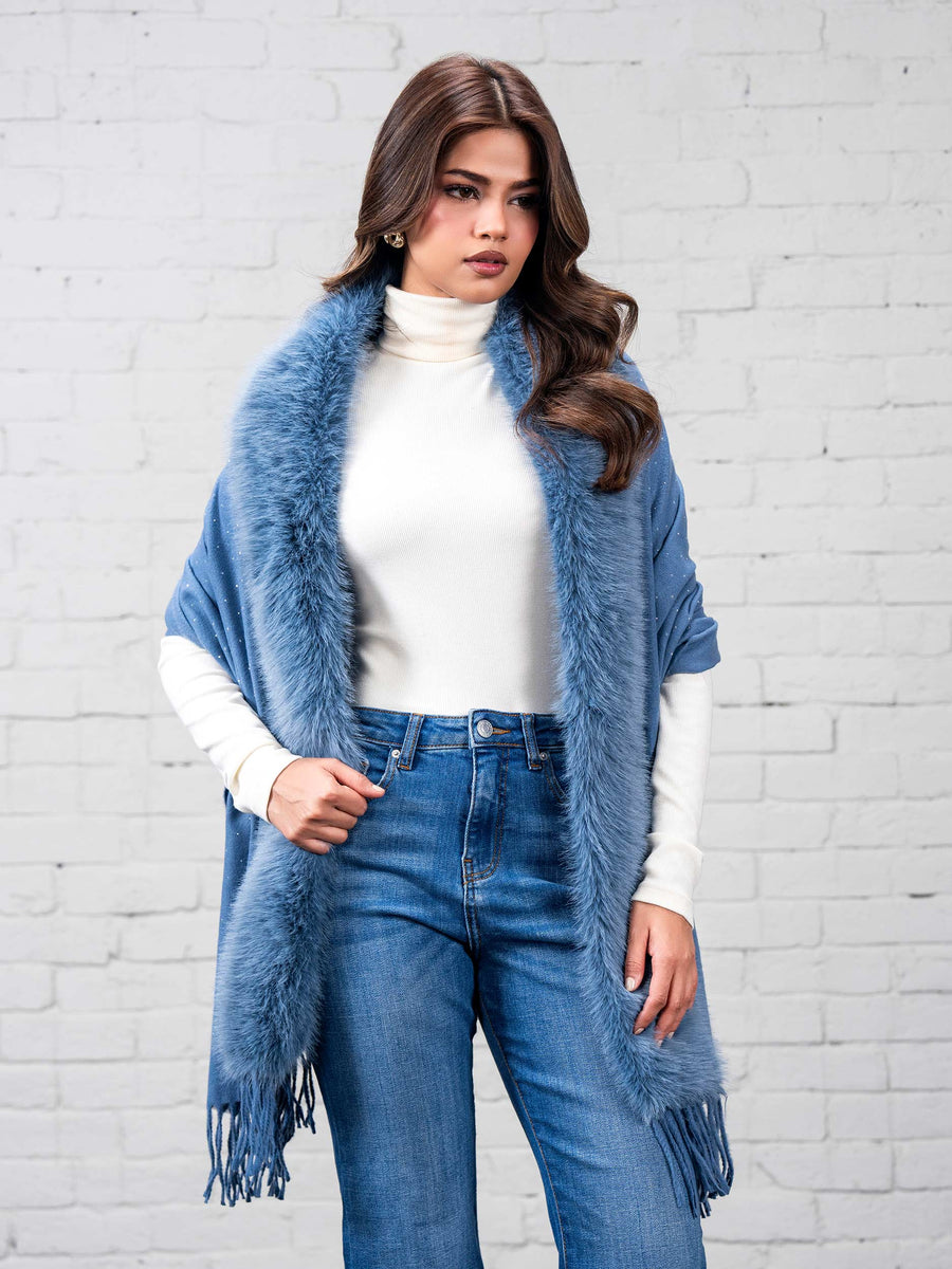 Close-up front view of woman wearing sky blue wool cape with plush faux fur trim over white turtleneck and blue jeans