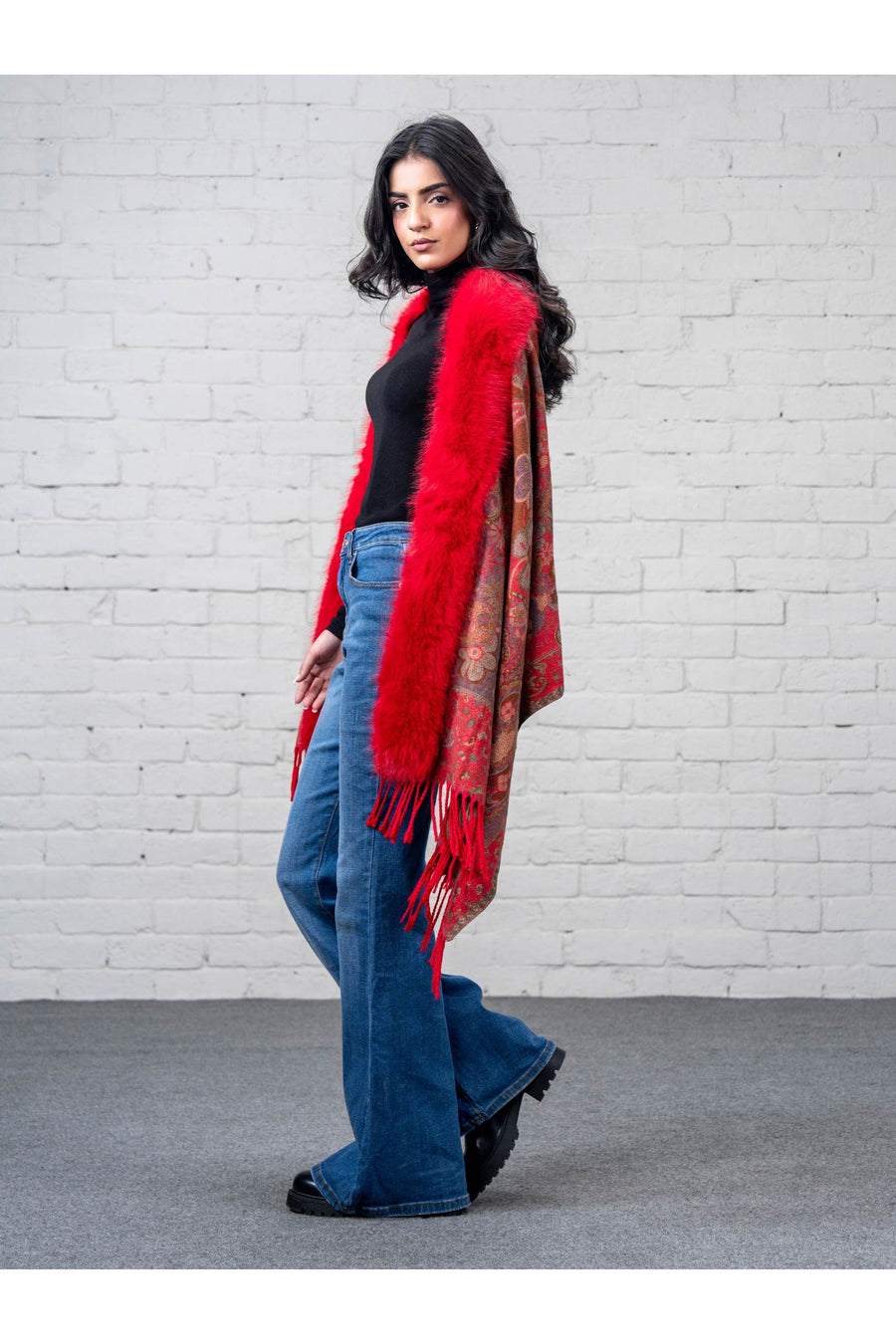 Side profile of a woman modeling the merino wool cape featuring floral paisley prints on a red base and fringed edges, showing the cape’s drape and flow.