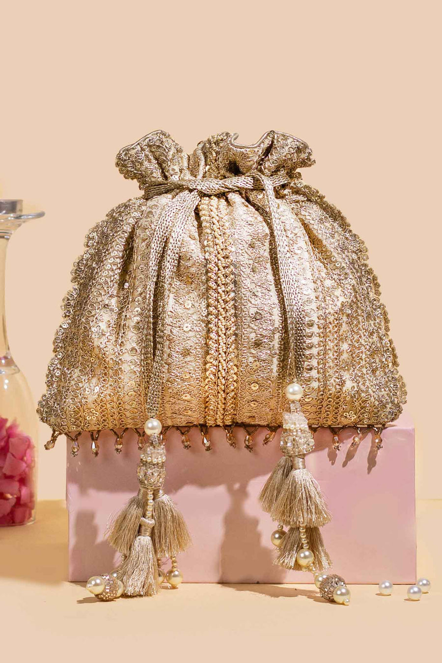 Gold embroidered potli bag with sequin embellishments and pearl tassels on a pastel background