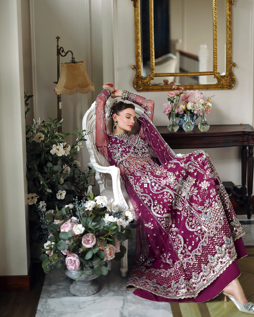 Close-up of woman reclining in white chair wearing richly embroidered magenta dress with pearl choker and bangles indoors