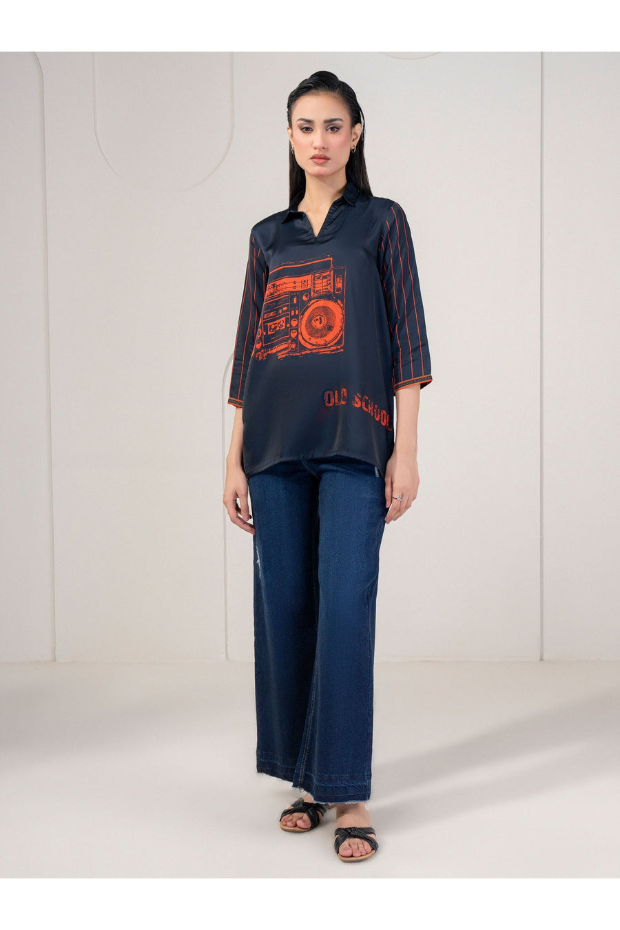 Full-length view of woman in navy silk top with orange retro print, standing.