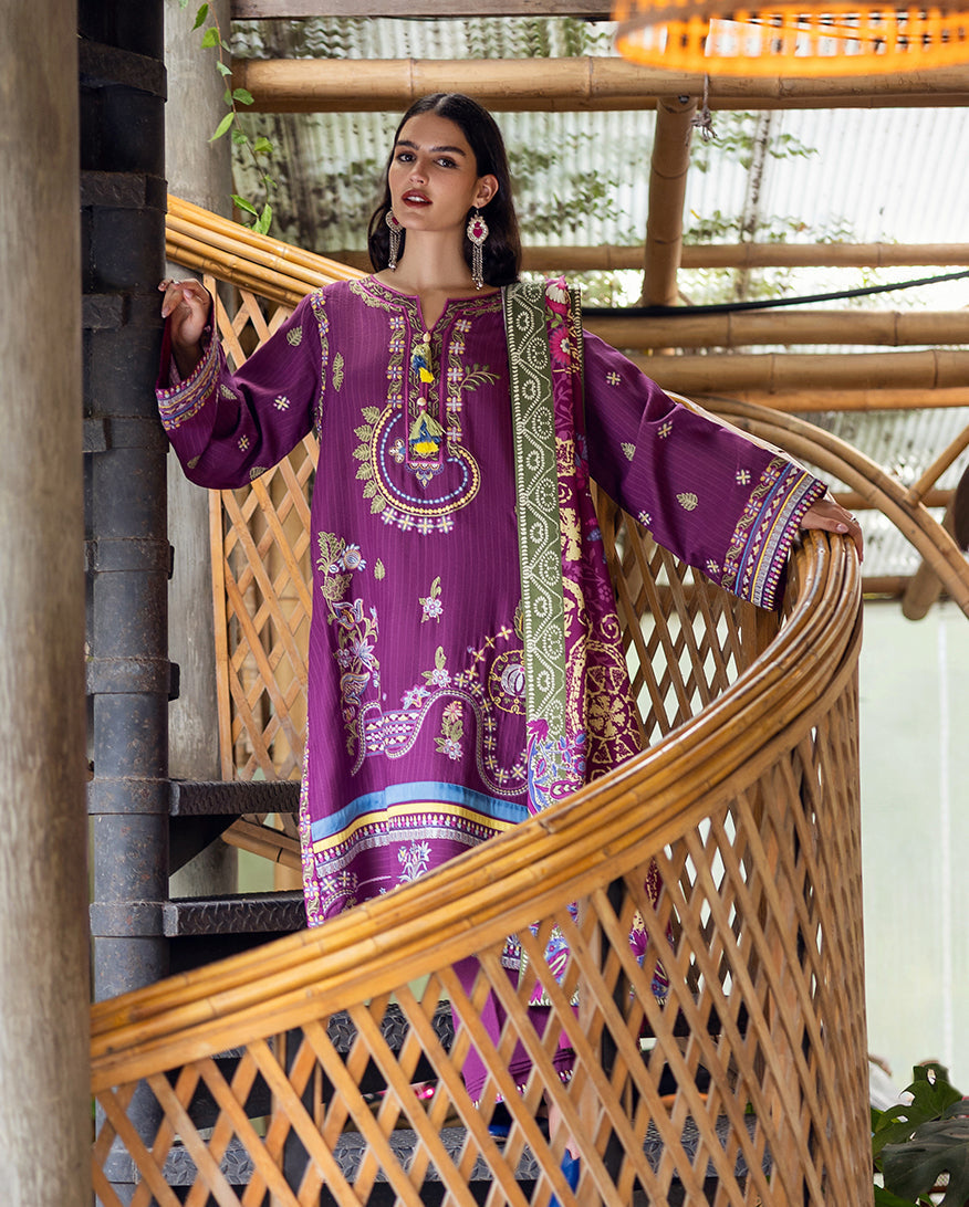 Model posing on staircase showcasing full length of embroidered purple Karandi suit and floral printed shawl.