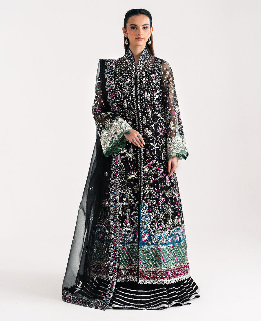 Full view of model wearing black embroidered organza formal suit with floral motifs, sheer sleeves, and striped lehenga